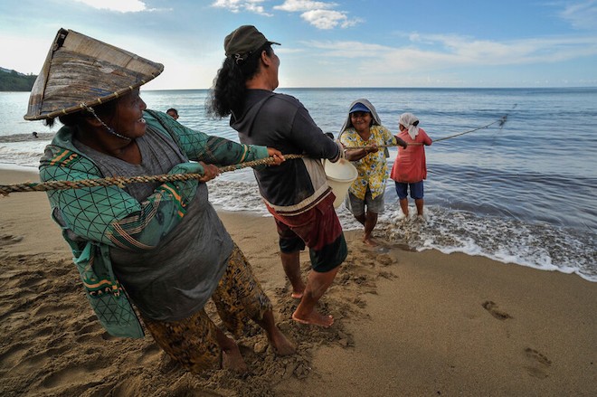 Community members in Indonesia helping to pull fishing nets on the shore.