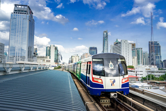 A railway train speeds through buildings in Thailand.