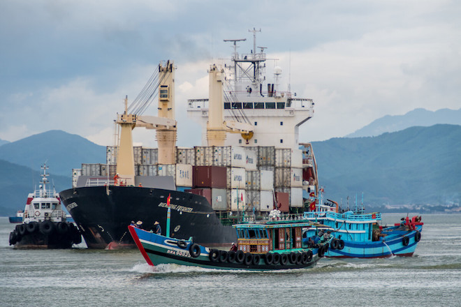 Tug boats circle a container ship calling at port in Viet Nam.
