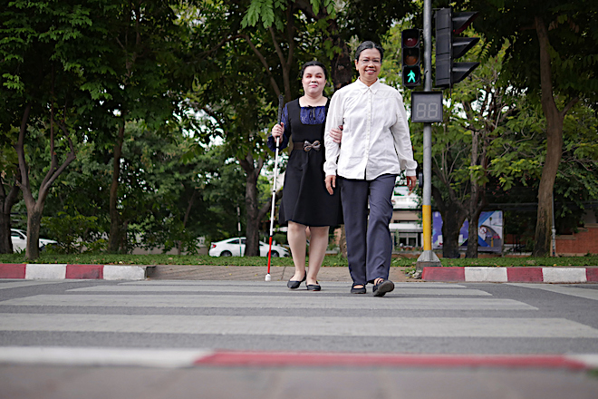 A visually impaired woman crossing the street with a guide.