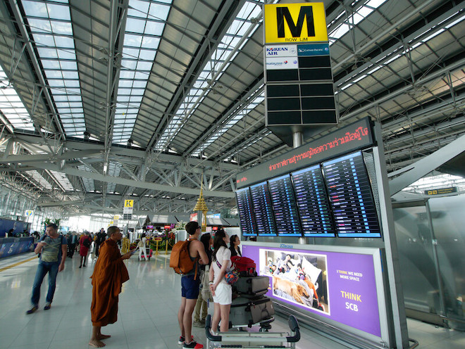 Tourists checking the departure and arrivals screens in an airport in Thailand.