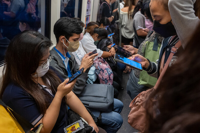 Commuters use their mobile phones on a crowded Skytrain in Bangkok.