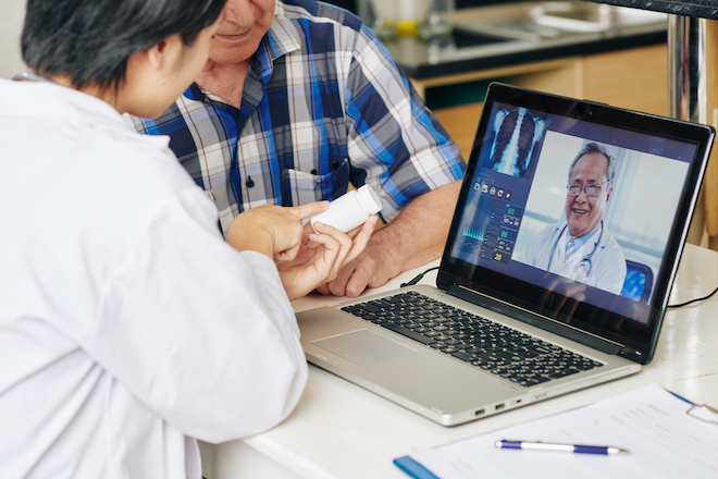 A doctor talking to a patient during a video call while a nurse assists in person. 
