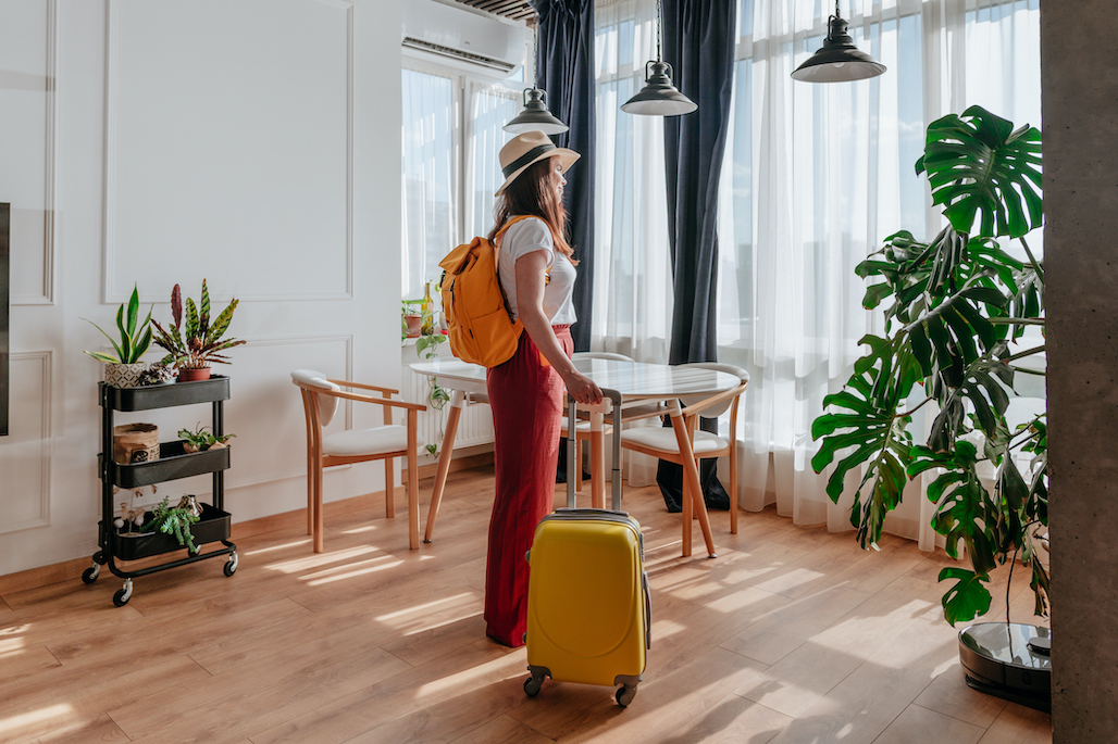A woman stands in a guest room with her luggage.