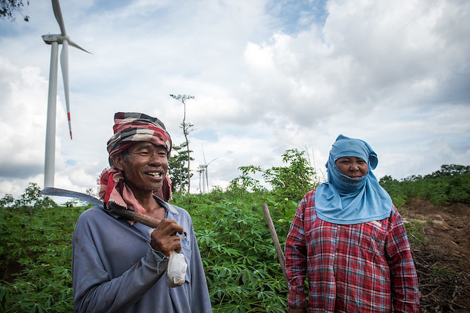 A wind turbine towers over farmers in Thailand.