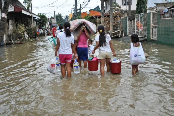 Children carrying personal items through flooded streets
