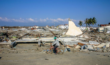 A man on a bicycle passes by a typhoon-damaged neighborhood in Indonesia. 