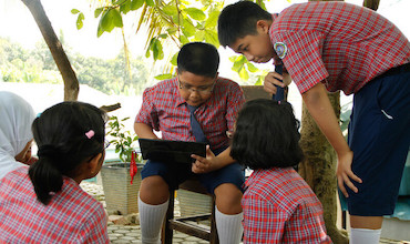 Students huddle around a classmate working on a laptop.
