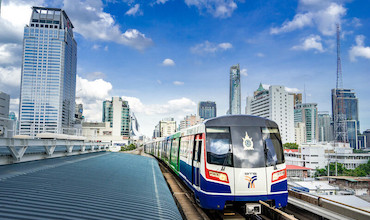 A railway train speeds through buildings in Thailand.
