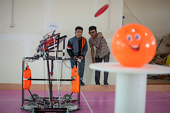 A student and his professor calibrate settings of a frisbee-shooting robot at the Batam State Polytechnic in Indonesia.  