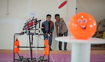 A student and his professor calibrate settings of a frisbee-shooting robot at the Batam State Polytechnic in Indonesia.