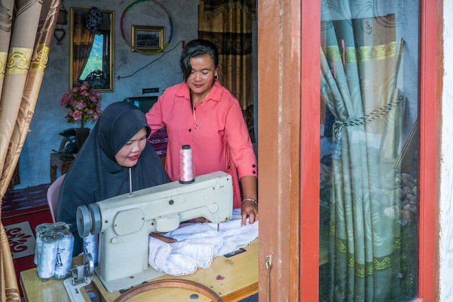 A woman supervising her employee who is sewing garments for sale in Indonesia.