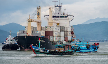Tug boats circle a container ship calling at a port in Viet Nam.