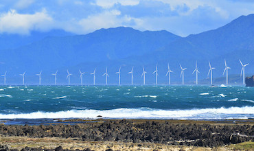 A line of wind turbines are seen from the shore.