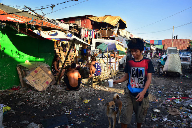 A boy plays with a dog with shanties in the background 