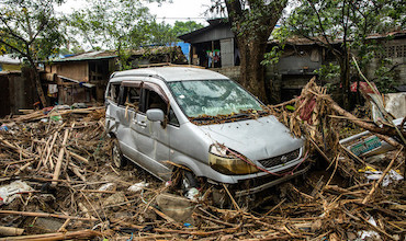 A damaged car sits on a ground strewn with typhoon debris.