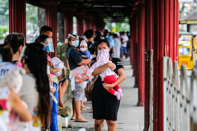 A woman cradles her infant while queueing up for the baby's vaccination.