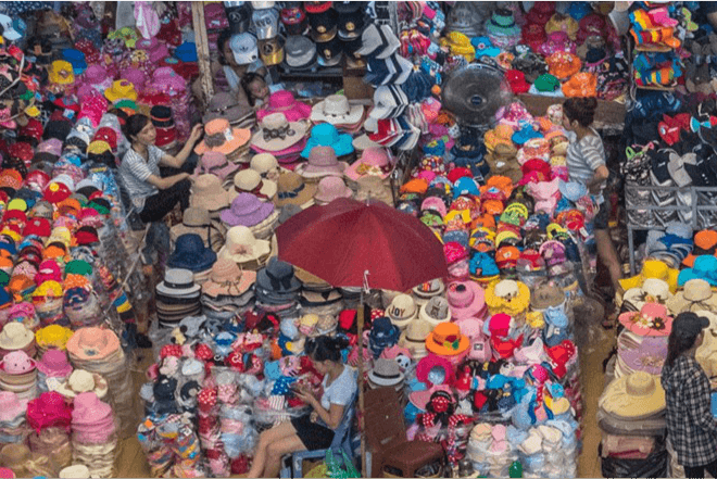 Vendors sit amid goods displayed in a commercial establishment.