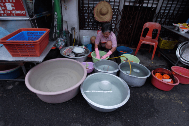 A woman washing dishes using water collected in basins.