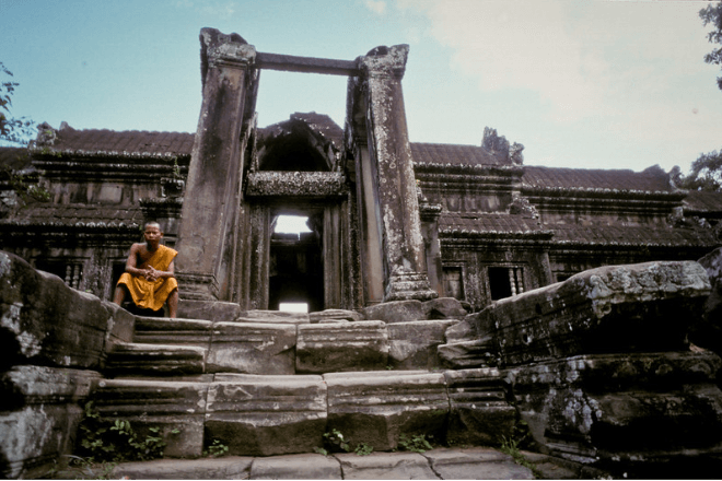 A monk sits on the steps of a temple.