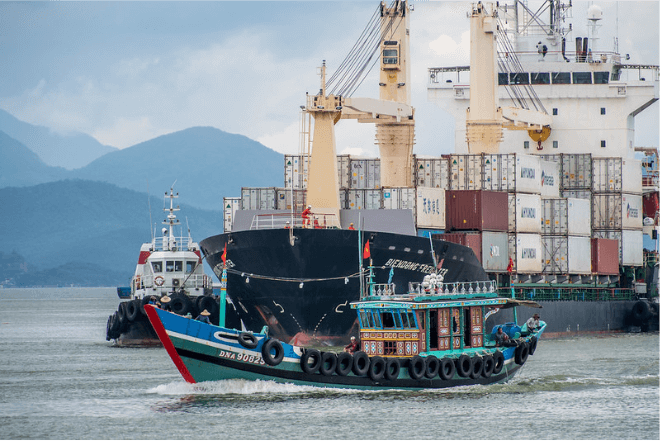Tugboats sail close to a container ship.