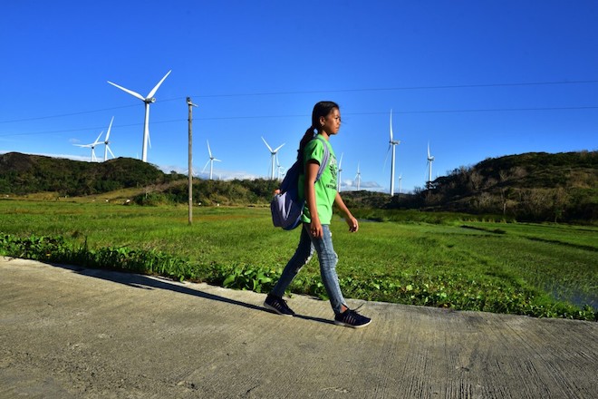 A girl walking past a wind farm.