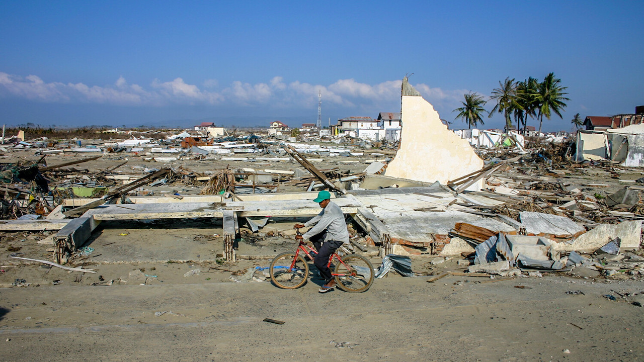 A man bikes against a backdrop of damaged houses and structures razed by a tsunami in Indonesia.