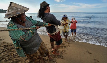 Community members in Indonesia helping to pull fishing nets on the shore.