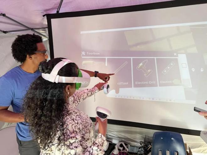 A man and a young girl with a VR headset look at a computer display.